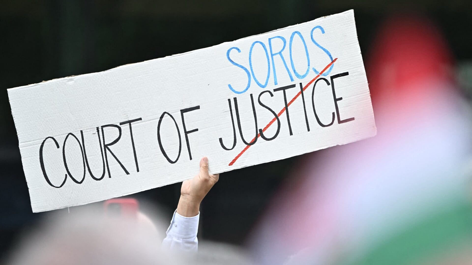 A participant displays a placard reading 'Court of (George) Soros' as members and supporters of the ruling FIDESZ party demonstrate in front of the European Commission's local headquarters in Budapest on 14 June 2024