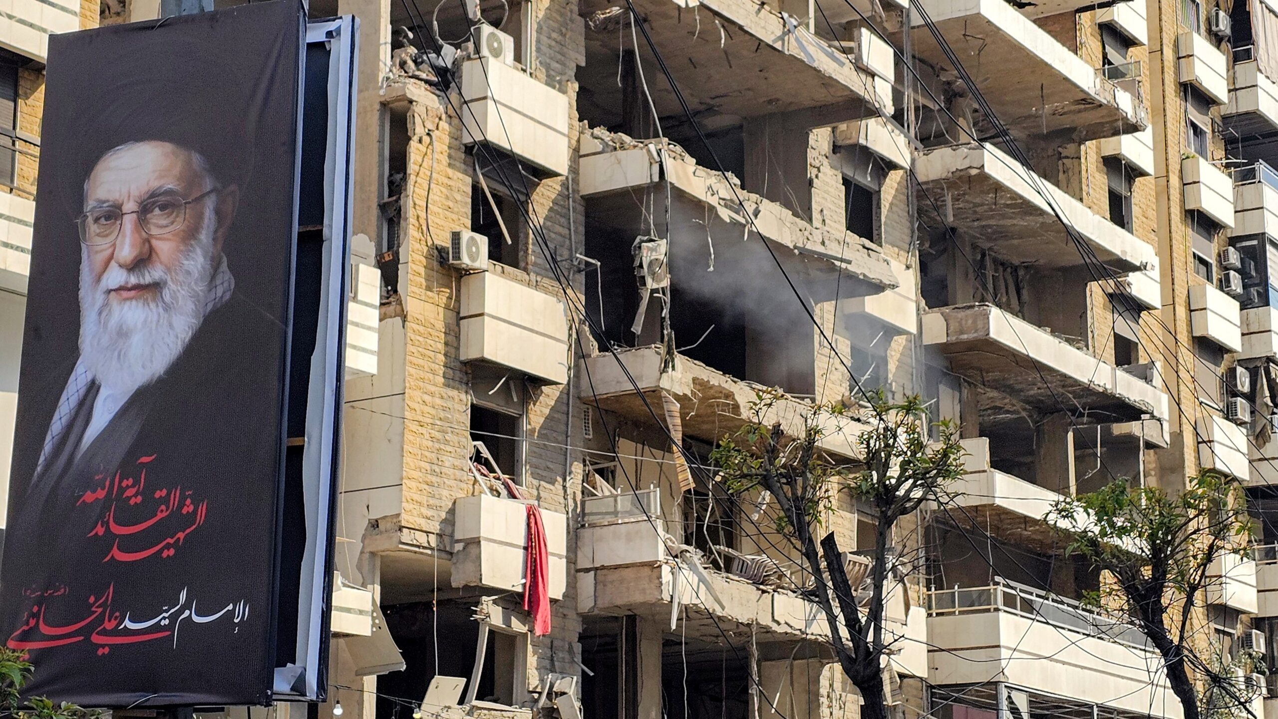 banner of Iran’s supreme leader Ayatollah Ali Khamenei is seen next to a building damaged by an Israeli strike in the southern suburbs of Beirut on March 3, 2026.