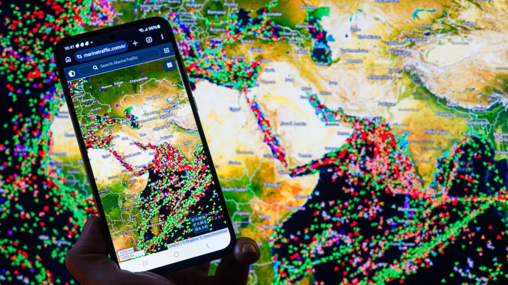 A MarineTraffic map showing ship movements in the Strait of Hormuz is displayed on a smartphone screen with a map in the background in this photo illustration, as commercial vessel traffic through the key oil shipping lane decreases amid the ongoing conflict involving Iran.