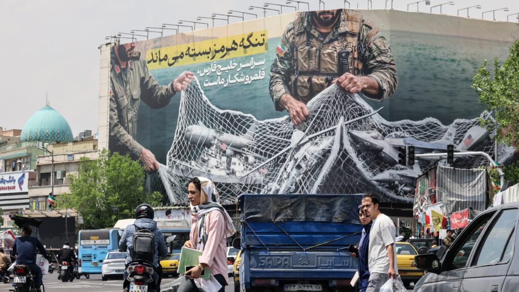 Iranian walks past a giant billboard reading 'The Strait of Hormuz remains closed' at the Revolution Square in Tehran on April 22, 2026, amid a ceasefire in the region.